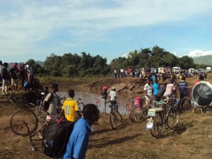 Crowd of people pushing bicycles and carrying goods across a muddy landscape
