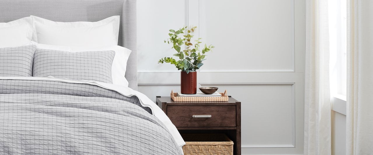 wooden bedside, vase with leaved branches, made up bed