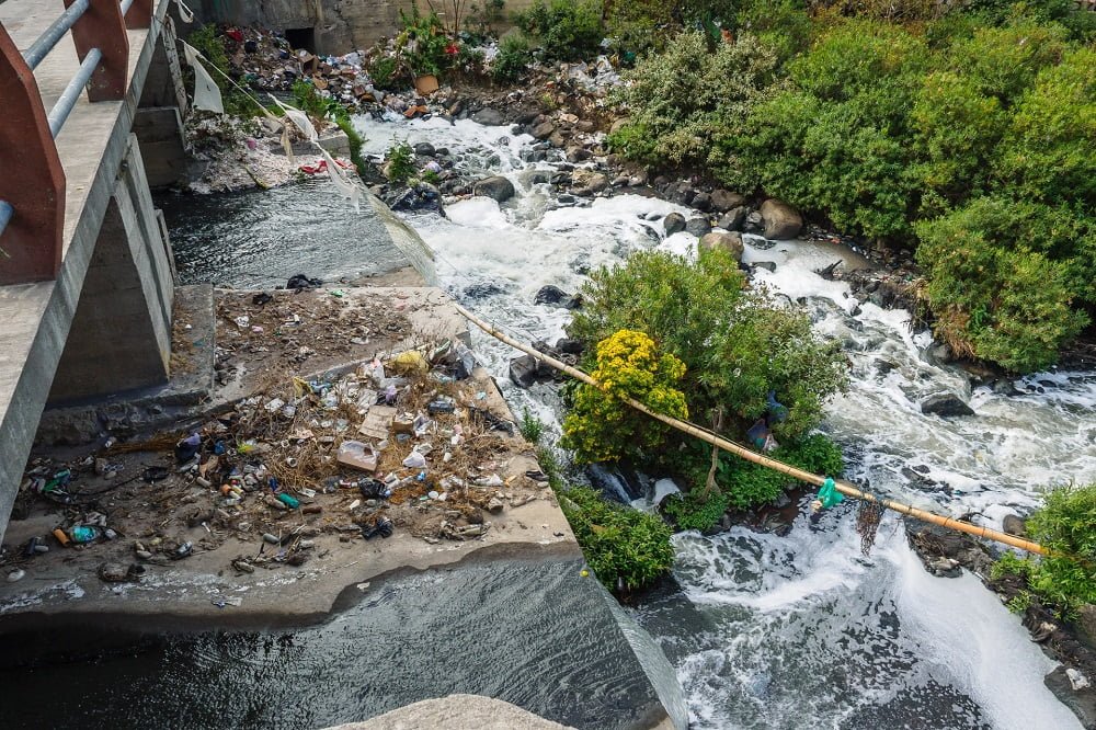 Hazardous Waste Management: heaps of domestic waste lying by a river below a bridge