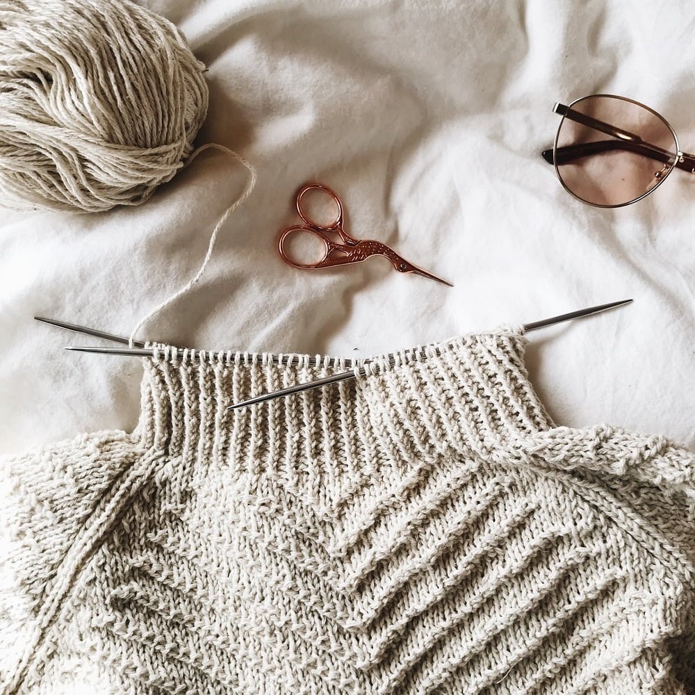 Stylish Ways to Make Your Wardrobe More Eco-Conscious: Scissors, yarn, gloasses, and  a jumper being knitted