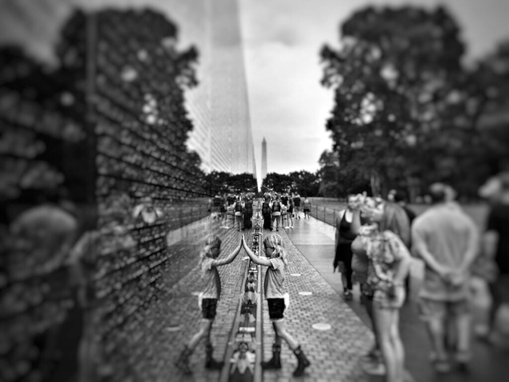 VA benefits - Vietnam Veterans Memorial: black and white photo of a child placing their hand on the memorial wall