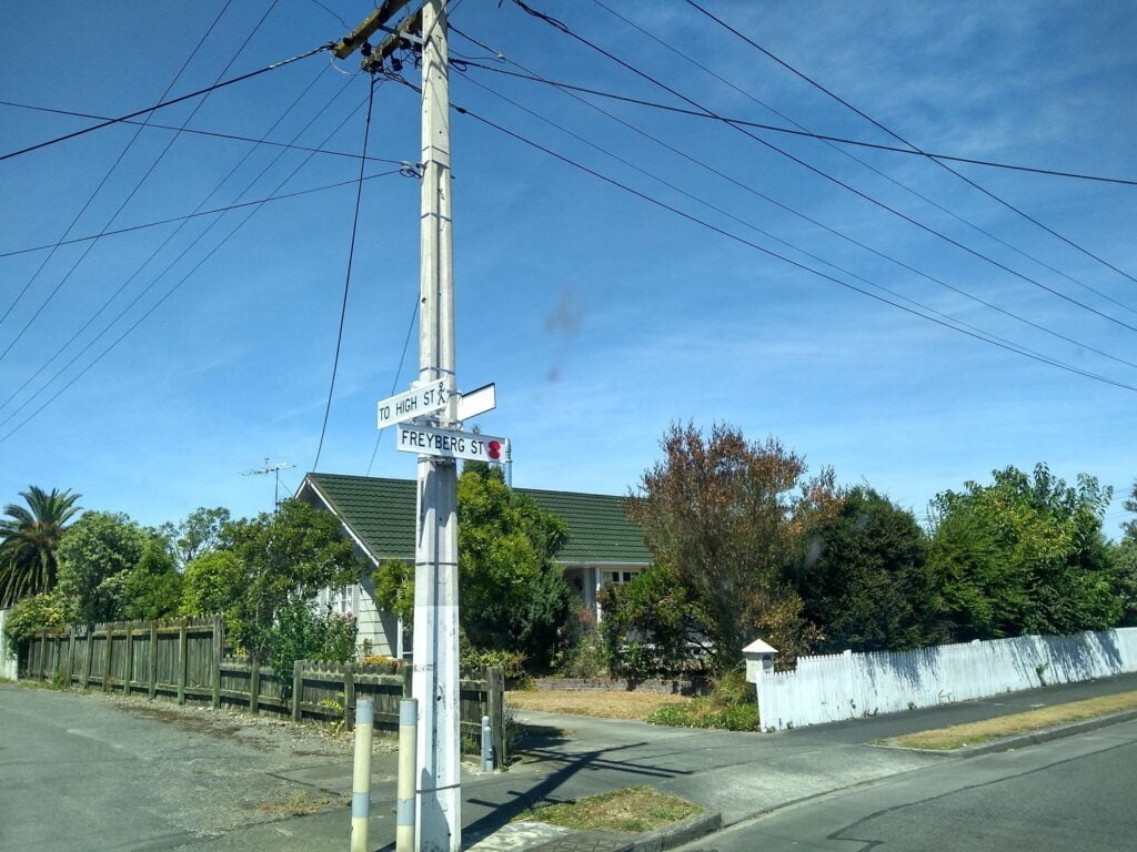 Power lines and street signs at an intersection with a house behind