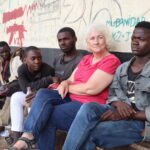 Carol McBrady sitting on a bench with 4 men under a graffitied wall