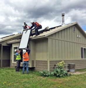 How to Prepare Your Roof for Solar Panels: Workmen in safety gear lifting a panel onto a residential roof