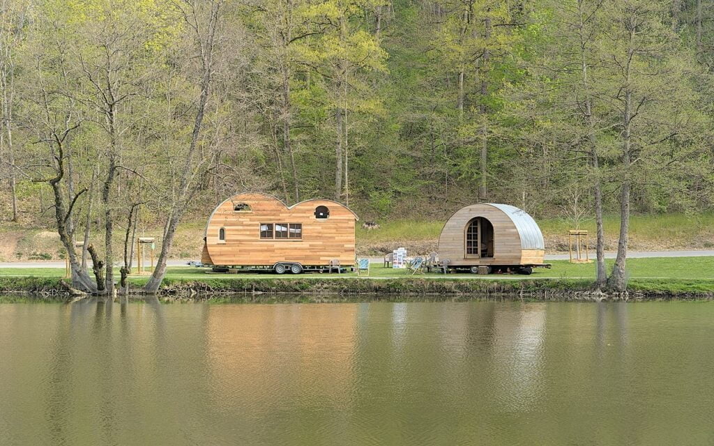 What Is Eco-Minimalist Architecture? Two wooden tiny houses on wheels by a lakeside under green trees.