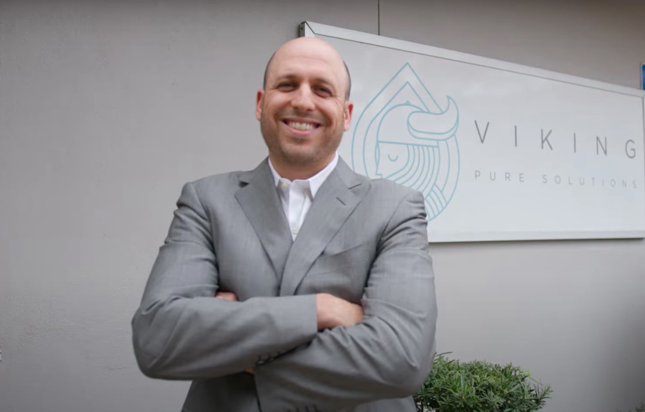 Man smiling in grey suit, with sign behind saying 'Viking"