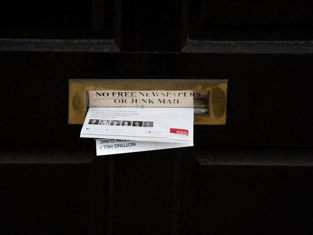 a bundle of junk mail sitting in a door mail slot with a sign saying "no free newspapers or junk mail"