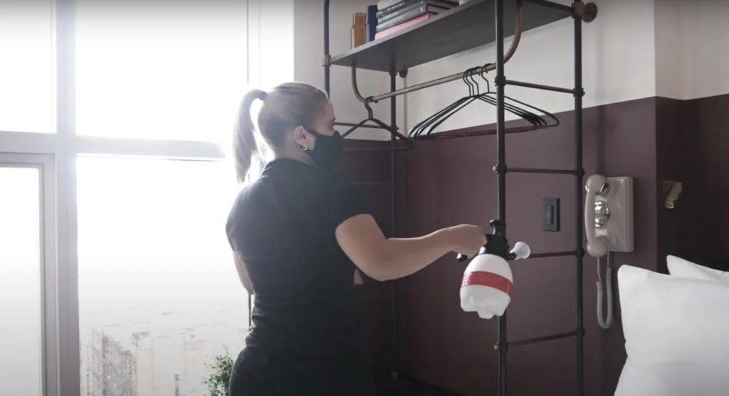 woman using cleaning product near telephone, wearing mask