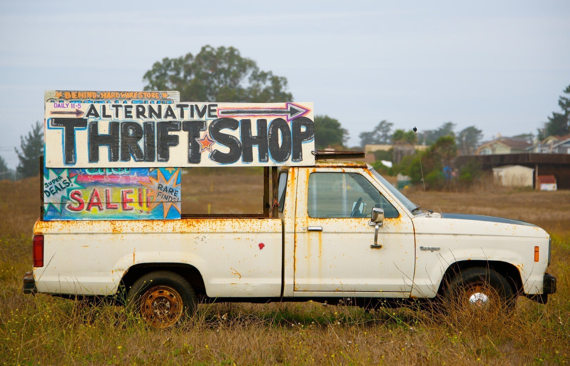 How to Begin Downsizing When You Want to Live Minimally: A white ute bearing a painted sign that says "Alternative Thrift Shop"