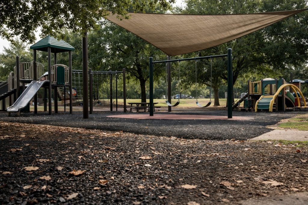 Public playground with rubber safety surfacing, partial shade sail, and open sightlines in a community park
