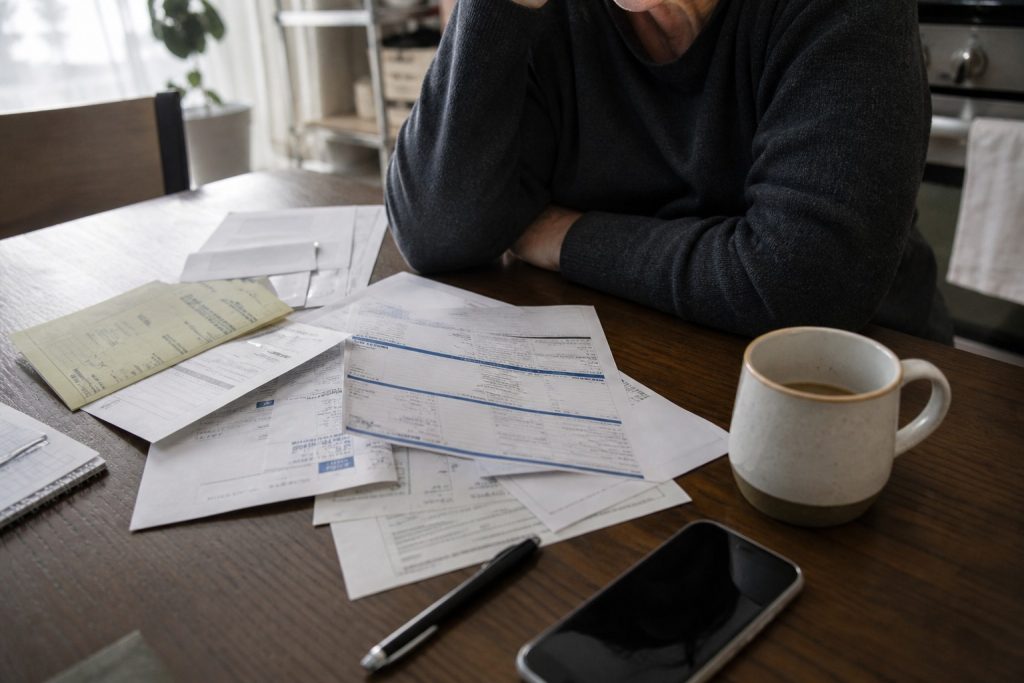 Medical bills and an insurance statement spread across a kitchen table beside a coffee mug and phone.